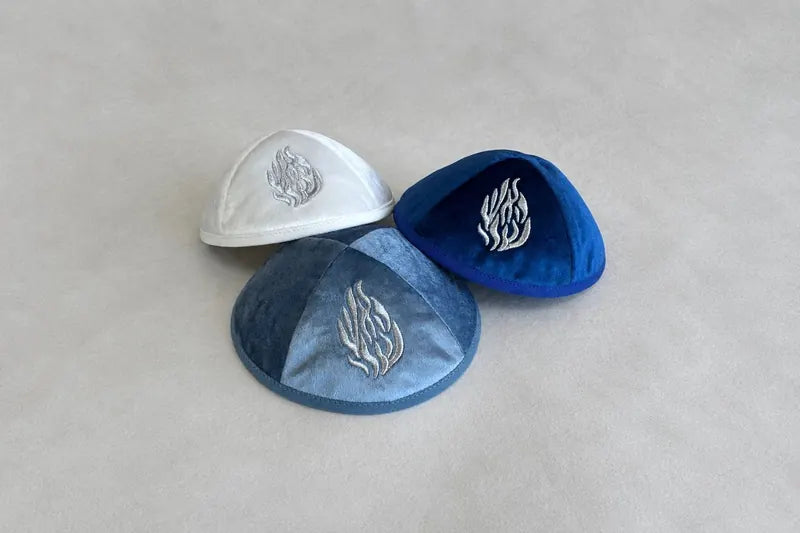 Symbole de flamme brodé en fil argenté, décliné sur trois teintes de velours — le même emblème, reproduit à l'identique sur toute la commande.