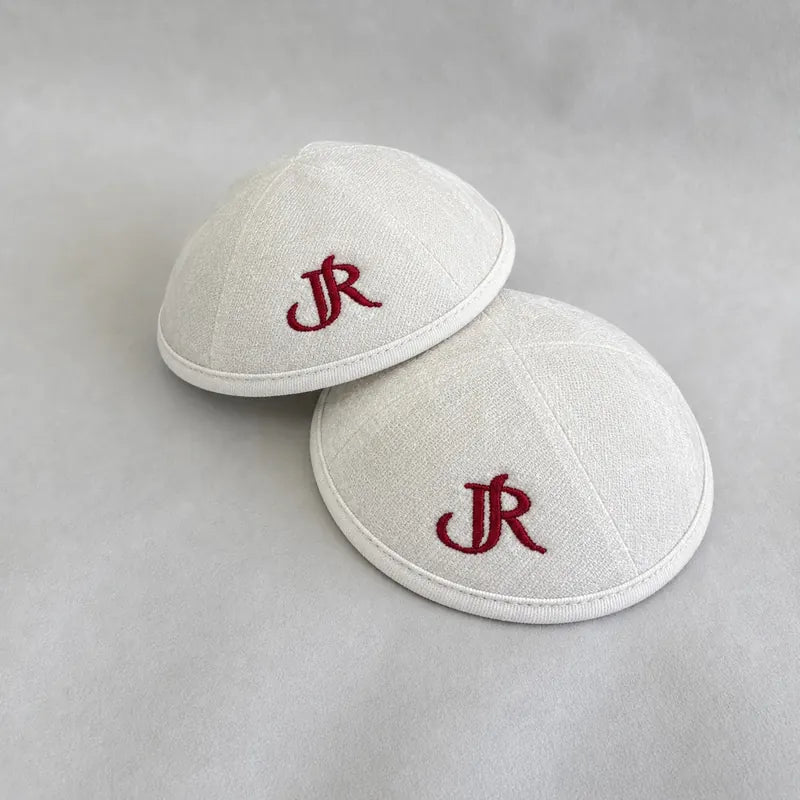 Monogramme "JR" brodé en fil bordeaux sur des kippot blanches, dans un style calligraphique.