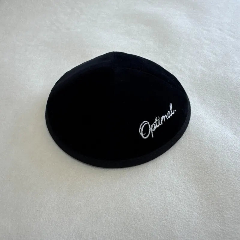 Signature "Optimal." brodée en fil argenté sur velours noir — une personnalisation d'entreprise discrète et élégante.