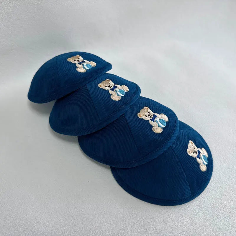 Petit ourson brodé en fil beige, répété à l'identique sur un lot en velours côtelé bleu nuit — idéal pour une naissance ou un Chabbat bébé.